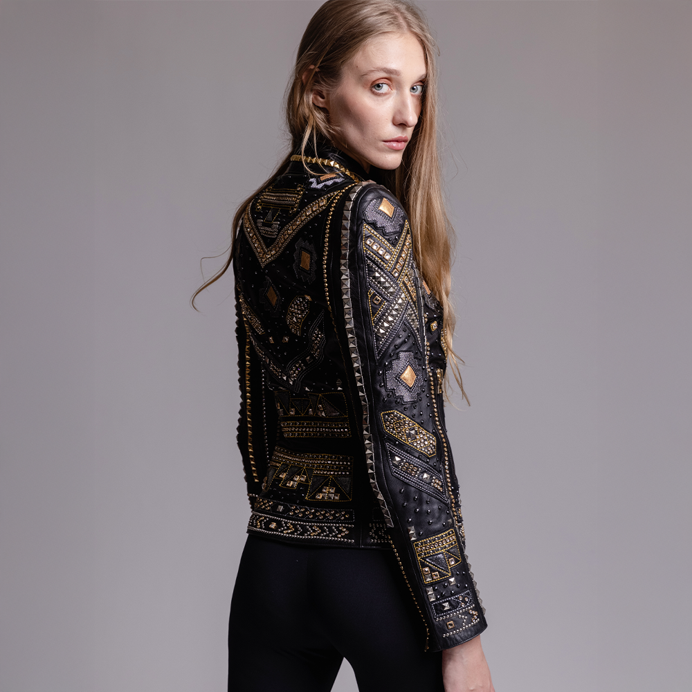 Woman wearing an ornate black and gold jacket against a gray background